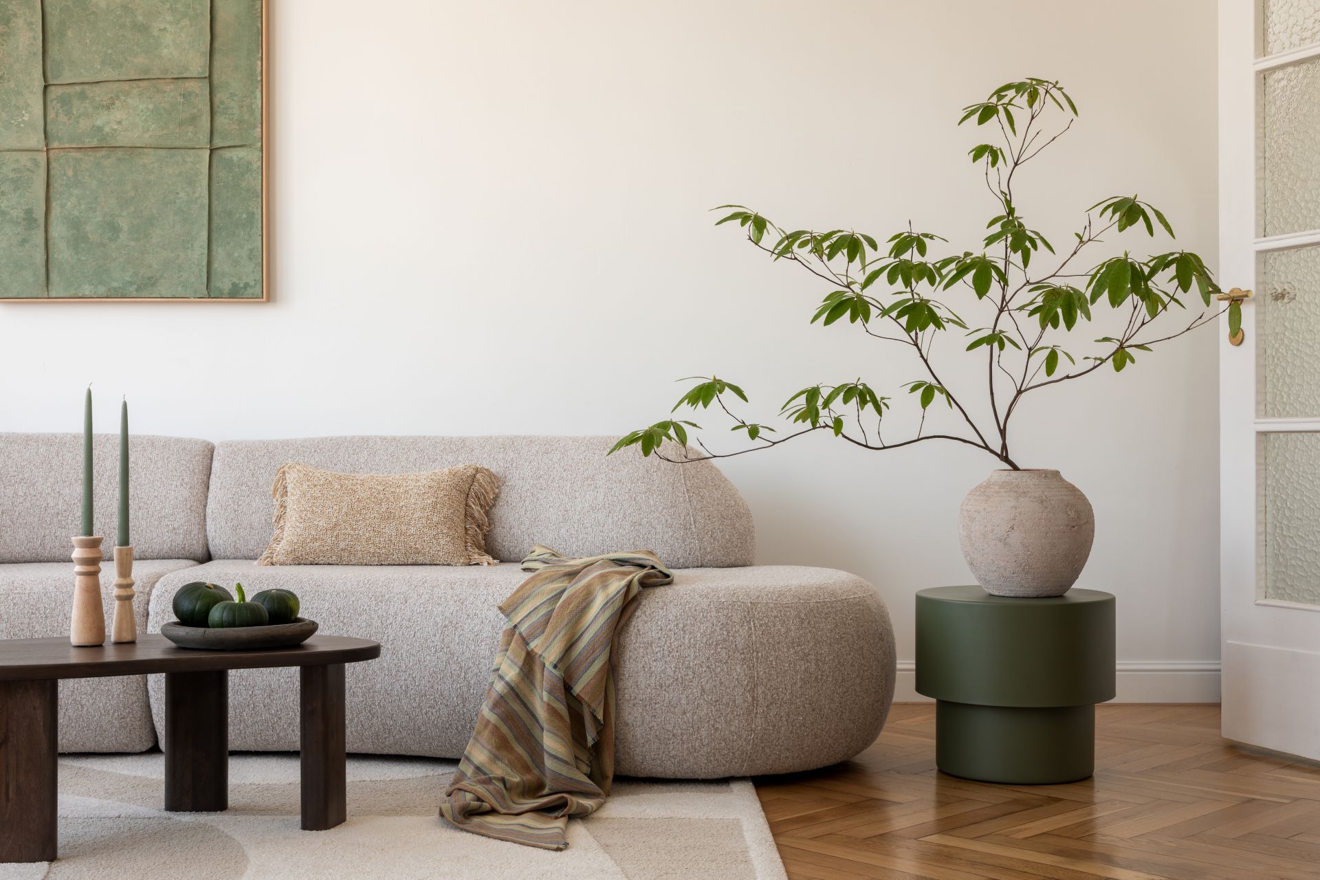 Helles Wohnzimmer mit runder Couch, grossen Pflanzen und natuerlichen Materialien als stilvolle Inspiration fuer das Einrichten rund um einen Specksteinofen.